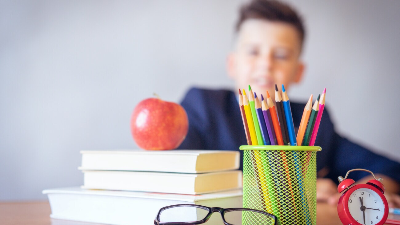 Boy in school uniform with books, pencils, glasses, clock and an apple.
