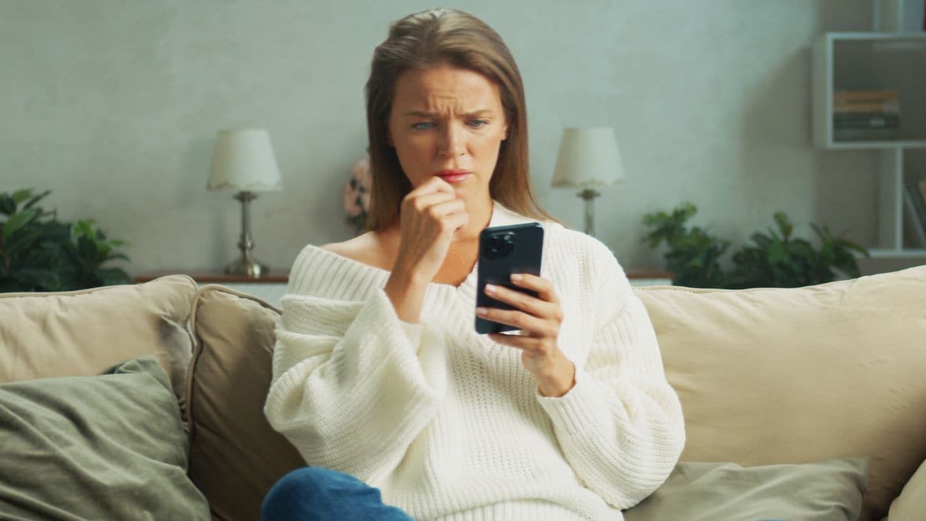 A woman looking concerned at a phone while sitting on a couch