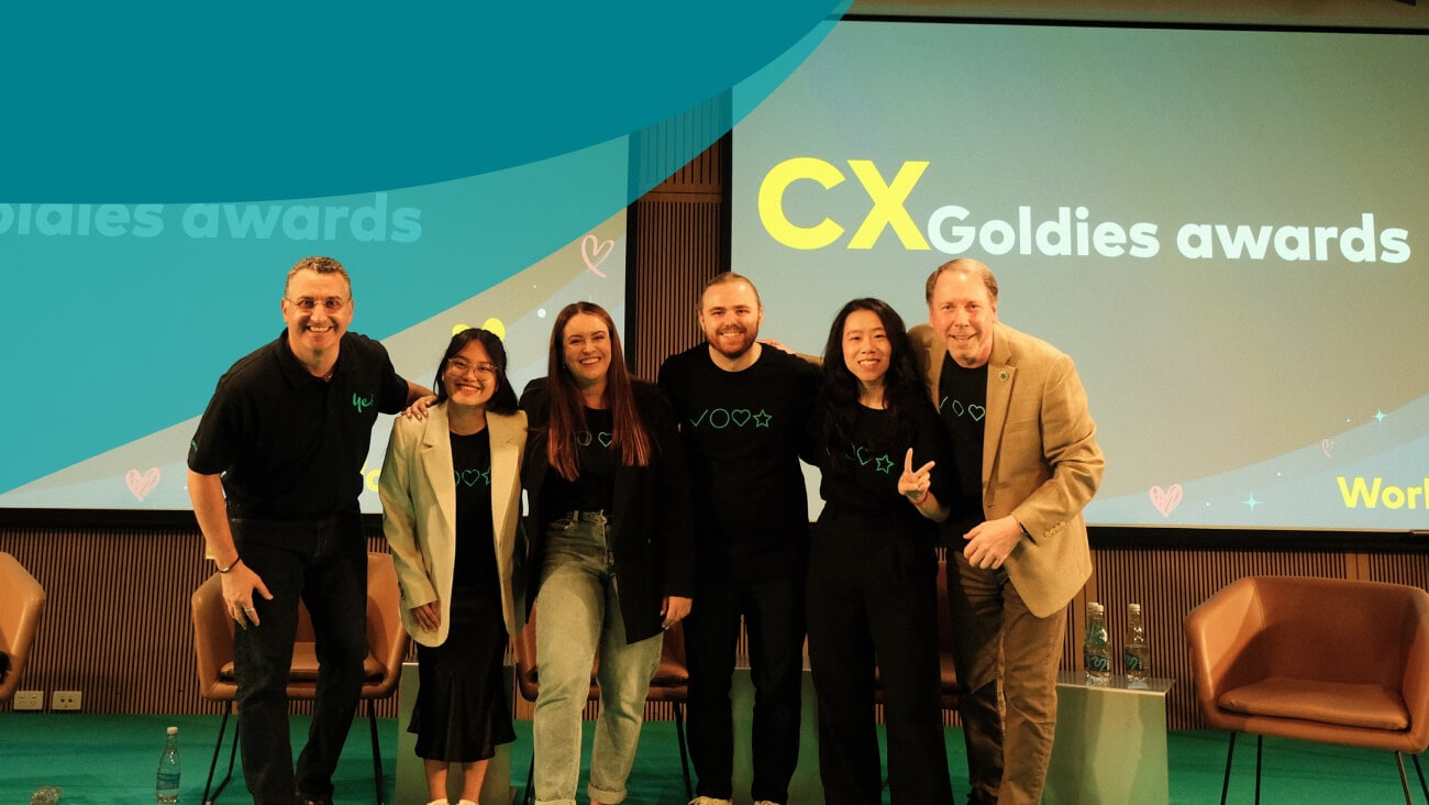 Optus CX Team smiling on stage in front of a screen that says ‘CX Goldies Awards’.