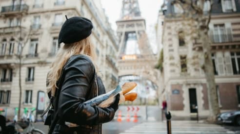 Girl in a beret carrying a baguette looking at the Eiffel Tower