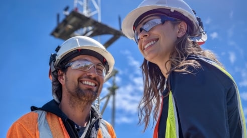 male and female Optus employees wearing hard hats with a network tower in background male and female Optus employees wearing hard hats with a network tower in background