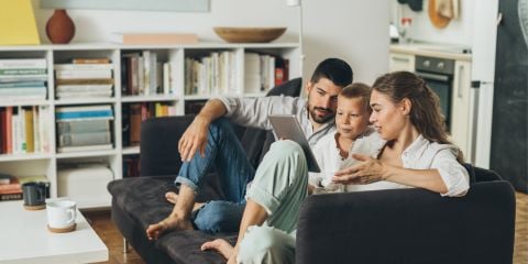 Father, child and mother sitting on a lounge looking a tablet the child is holding.